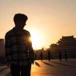 man in black and white plaid dress shirt standing on brown wooden floor during sunset