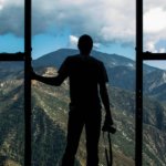 silhouette photo of person standing near door overlooking mountain during daytime