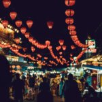 people walking between food stalls under chinese lanterns