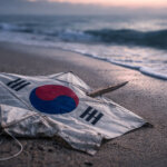 South Korean flag lying on a stormy beach as waves roll in, symbolizing Bitcoin surging past $71,000 during an 18% crash in South Korea’s stock market