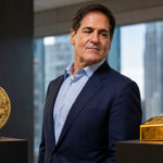 Mark Cuban standing between Bitcoin and gold displays inside a corporate office as investors debate crypto’s role as a long-term monetary hedge