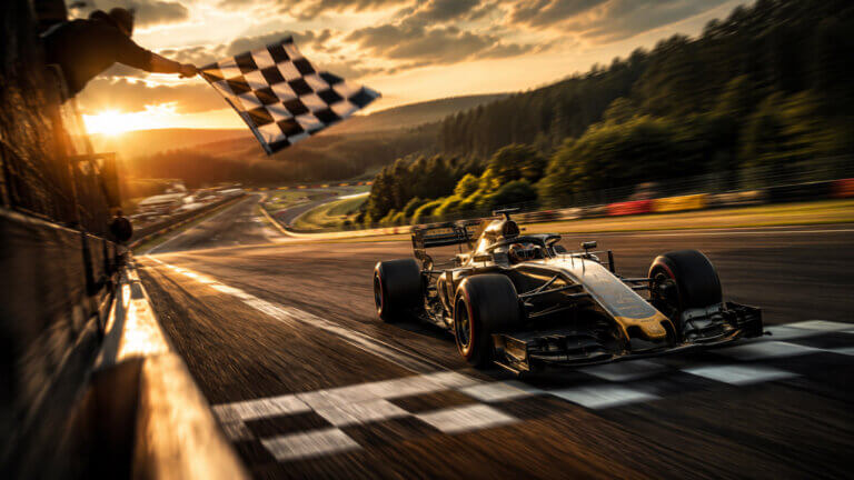 Formula racing car crossing the finish line beneath a waving checkered flag on the Belgian circuit at golden hour.