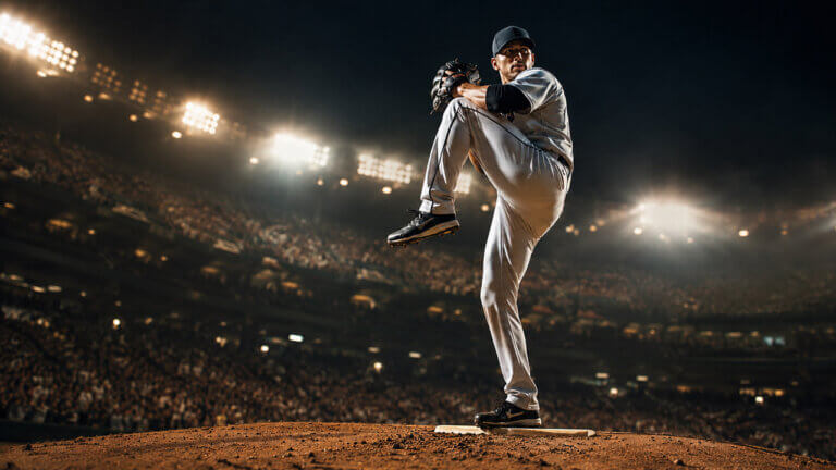 American League pitcher delivering a high-leg windup on the mound beneath bright stadium lights.
