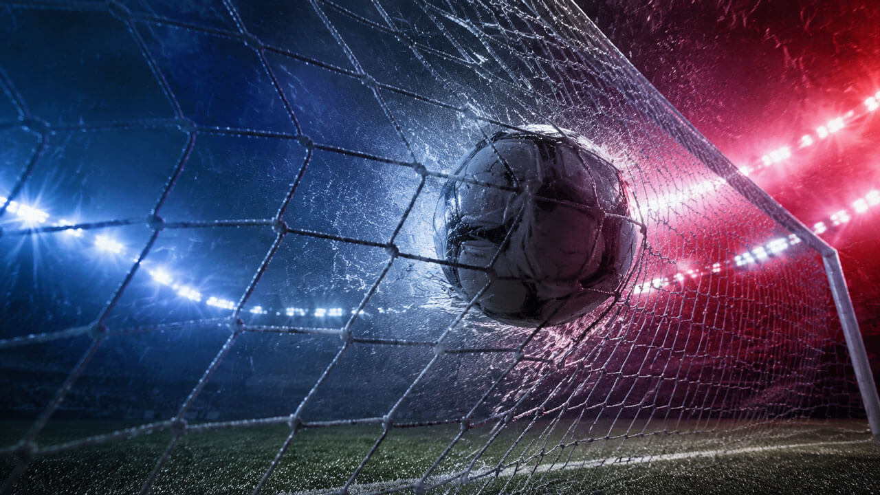 Football streaks toward the goal through heavy rain as red-blue and claret-blue lighting divides the dramatic stadium scene.